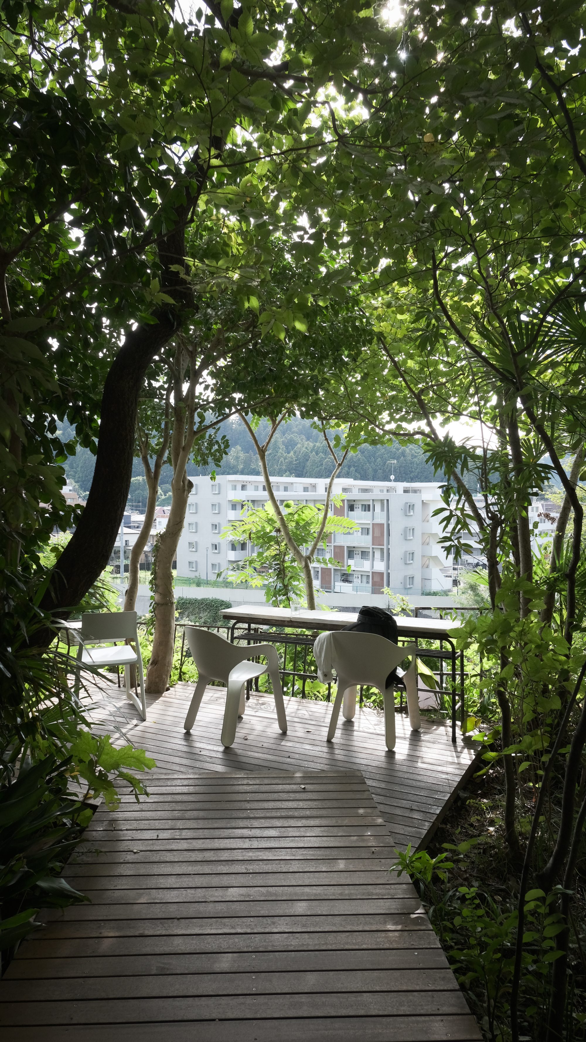 Trees looking like a photo frame. A white table and two chairs on a terrace in the middle.